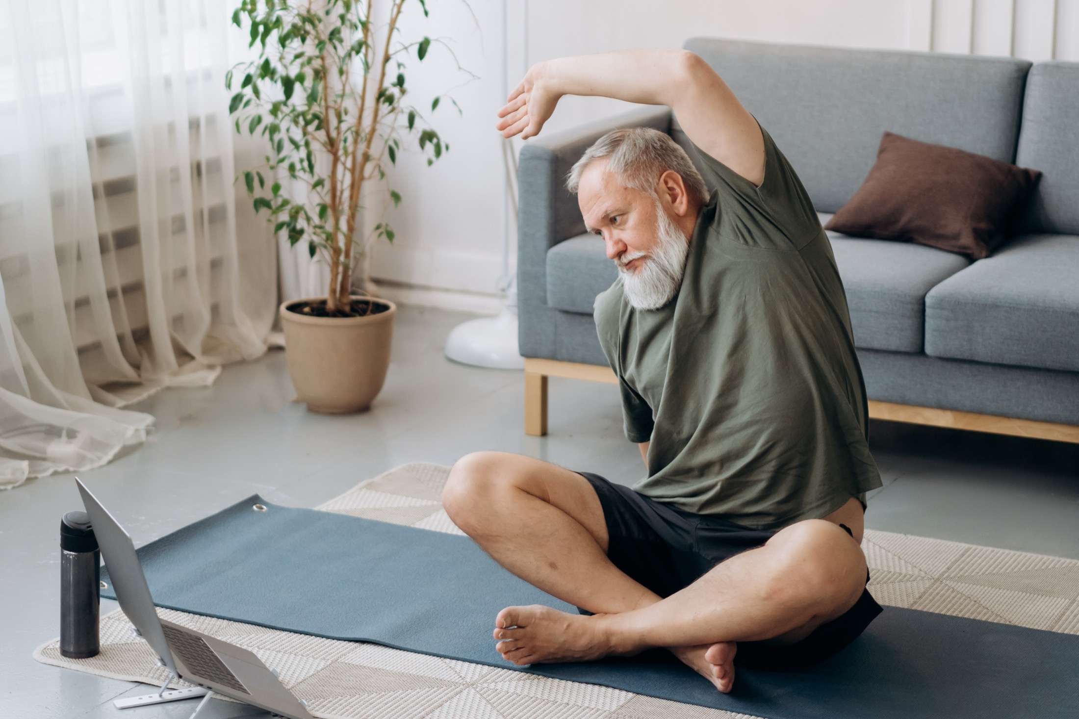 Active older man stretching at home with an online movement lesson nearby