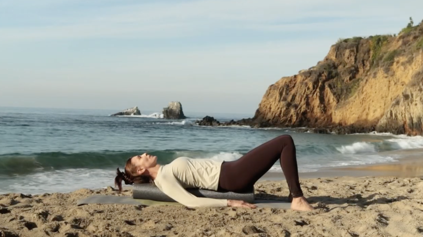 Alicia Gilbert lying on a foam roller on the beach during a nervous system reset